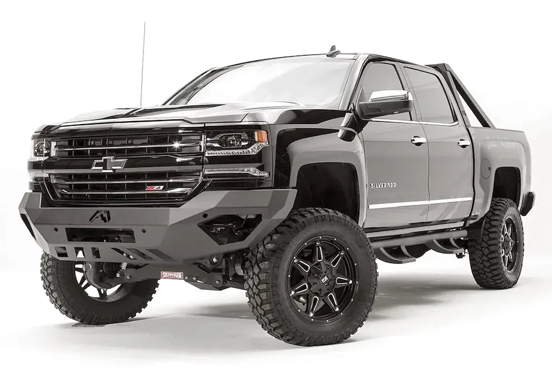 Fab Fours Vengeance front bumper on a black lifted Chevrolet Silverado 1500, front driver-side three-quarter view, showing the no-guard design, angular end wings and slotted skid plate