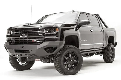 Fab Fours Vengeance front bumper on a black lifted Chevrolet Silverado 1500, front driver-side three-quarter view, showing the no-guard design, angular end wings and slotted skid plate