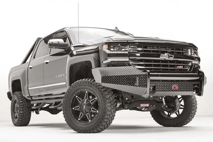 Fab Fours Black Steel front bumper on a black lifted Chevrolet Silverado 1500, front passenger-side three-quarter view, showing the diamond-plate end wing, mesh vent and red logo plate