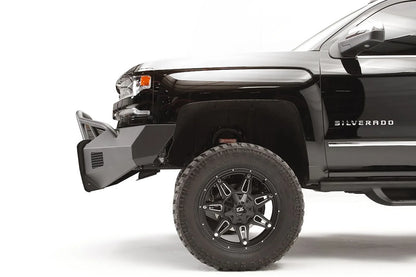 Fab Fours Elite front bumper with pre-runner guard on a lifted black Chevrolet Silverado 1500, driver-side profile, showing the angular bumper end and tubular guard ahead of the front wheel