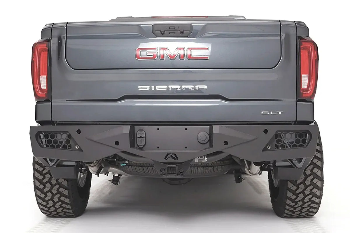 Fab Fours Vengeance rear bumper on a gray GMC Sierra 1500, straight-on rear view, showing the honeycomb light pockets, center hitch receiver opening, and angular plated face