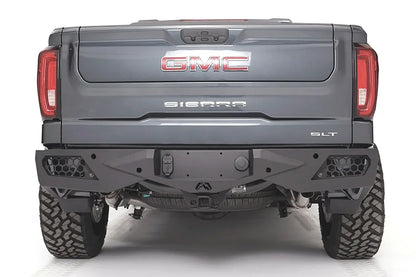 Fab Fours Vengeance rear bumper on a gray GMC Sierra 1500, straight-on rear view, showing the honeycomb light pockets, center hitch receiver opening, and angular plated face