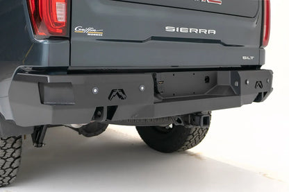 Fab Fours Premium rear bumper on a gray GMC Sierra 1500, close rear three-quarter view, showing the plate recess, end-cap logos, and hitch receiver