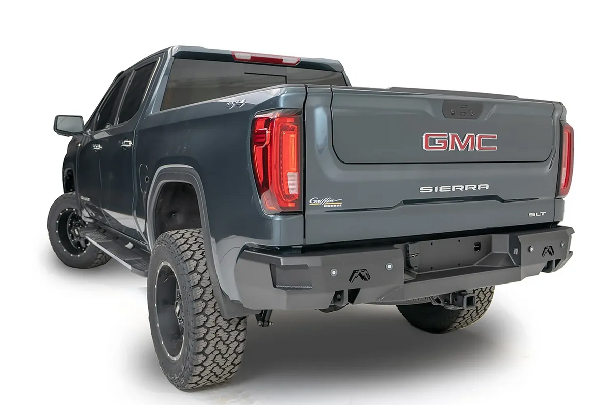 Fab Fours Premium rear bumper on a gray GMC Sierra 1500, rear driver-side three-quarter view, showing the angular end caps, Fab Fours logos, and hitch receiver