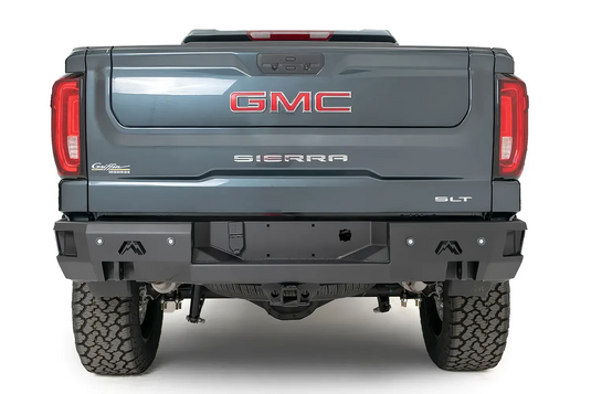 Fab Fours Premium rear bumper on a gray GMC Sierra 1500, straight-on rear view, showing the center plate recess, Fab Fours logos, and integrated light openings