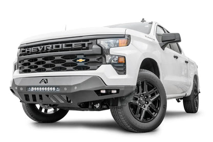 Fab Fours Vengeance front bumper on a white Chevrolet Silverado 1500, front driver-side three-quarter view, showing the LED light bar, cube light pods, and skid plate