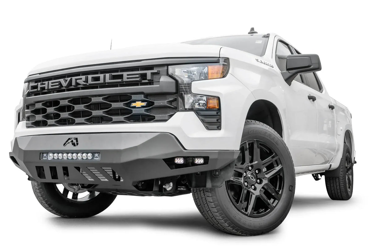 Fab Fours Vengeance front bumper on a white Chevrolet Silverado 1500, front driver-side three-quarter view, showing the LED light bar, angular bumper wing, and skid plate cutouts