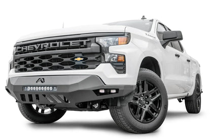 Fab Fours Vengeance front bumper on a white Chevrolet Silverado 1500, front driver-side three-quarter view, showing the LED light bar, angular bumper wing, and skid plate cutouts
