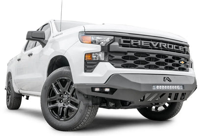 Fab Fours Vengeance front bumper on a white Chevrolet Silverado 1500, front passenger-side three-quarter view, showing the LED light bar, cube light pods, and slotted skid plate