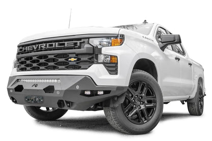 Fab Fours Matrix front bumper on a white Chevrolet Silverado 1500, low driver-side front three-quarter view, with LED light bar, cube lights, parking sensors, and winch fairlead