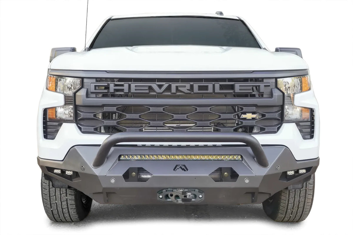 Fab Fours Matrix front bumper with pre-runner guard on a white Chevrolet Silverado 1500, front view, with LED light bar, dual cube lights in each corner, parking sensors, and winch fairlead