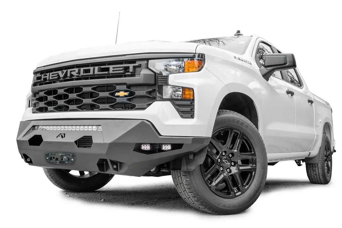 Fab Fours Matrix Front Bumper on a white Chevrolet Silverado 1500, front driver-side view, with the faceted steel bumper, LED light bar, cube lights and winch fairlead
