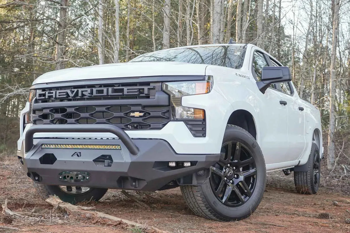Fab Fours Matrix Front Bumper with pre-runner guard on a white Chevrolet Silverado 1500 outdoors, front driver-side view, showing the angular steel bumper, tubular guard and LED light bar