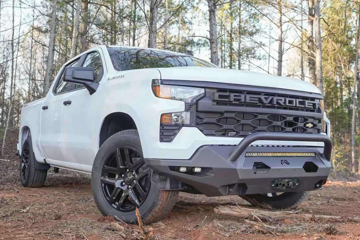 Fab Fours Matrix Front Bumper with pre-runner guard on a white Chevrolet Silverado 1500 outdoors, front passenger-side view, with the guard, center light bar, side cube lights and Fab Fours logo