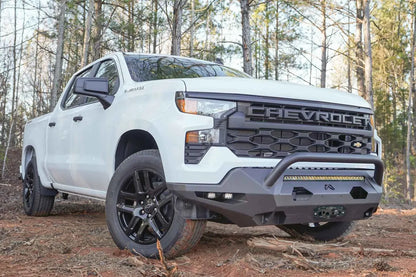 Fab Fours Matrix Front Bumper with pre-runner guard on a white Chevrolet Silverado 1500 outdoors, front passenger-side view, with the guard, center light bar, side cube lights and Fab Fours logo