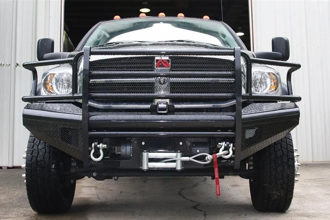 Fab Fours Black Steel front bumper with full guard on a black Ram 2500, straight-on front view, showing the full grille guard, diamond-plate face, winch with D-ring shackles