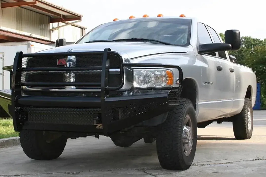 Fab Fours Black Steel front bumper with full guard on a silver Ram 2500, front passenger-side three-quarter view outdoors, showing the full grille guard, diamond-plate bumper end, and headlight hoop