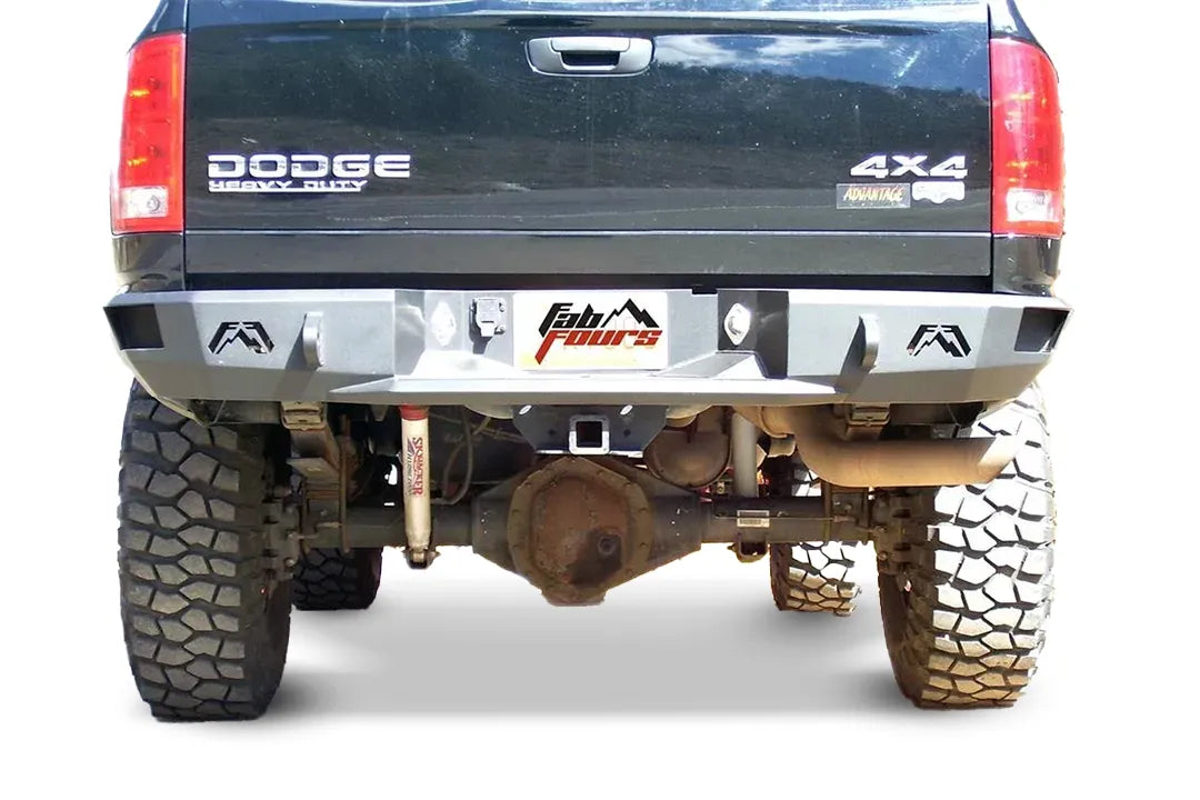 Fab Fours Premium rear bumper on a black Dodge Ram 2500, straight-on rear view, showing the Fab Fours logo end caps, center plate recess, and hitch receiver