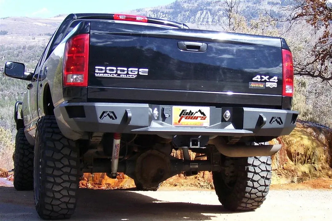 Fab Fours Premium rear bumper on a black Dodge Ram 2500, rear driver-side three-quarter view outdoors, showing the logo end caps, plate recess, and hitch receiver