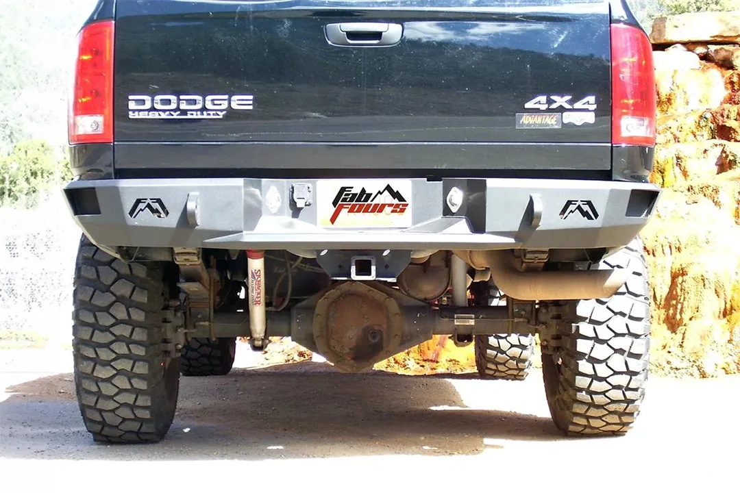 Fab Fours Premium rear bumper on a black Dodge Ram 2500, straight-on rear view outdoors, showing the Fab Fours logo end caps, center plate recess, and hitch receiver