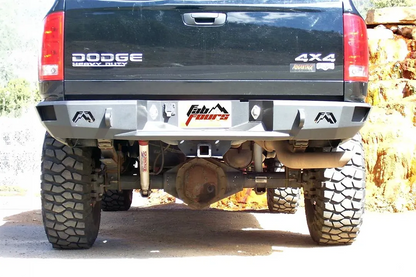 Fab Fours Premium rear bumper on a black Dodge Ram 2500, straight-on rear view outdoors, showing the Fab Fours logo end caps, center plate recess, and hitch receiver