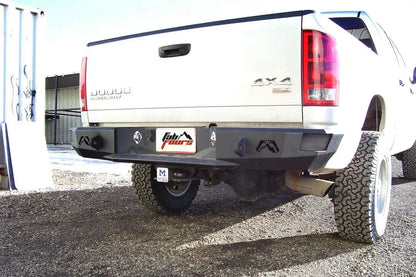 Fab Fours Premium rear bumper on a white Dodge Ram 2500, rear three-quarter view outdoors, showing the logo end caps, light cutouts, and plate recess
