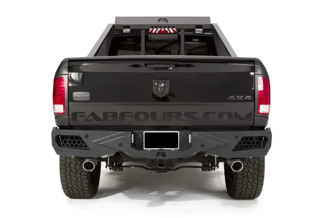 Fab Fours Premium rear bumper on a black Ram 1500 with chase rack, straight rear view, with honeycomb mesh light openings, center license plate mount, and hitch receiver