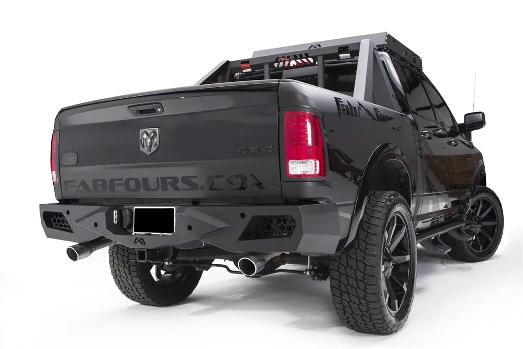Fab Fours Premium rear bumper with honeycomb mesh light openings on a lifted black Ram 1500 with chase rack and Fab Fours graphics, passenger-side rear three-quarter view, with hitch receiver and dual exhaust