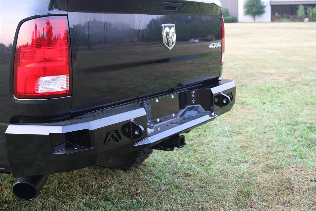 Fab Fours Premium rear bumper on a black Ram 1500, rear driver-side three-quarter view outdoors, showing the logo end cap, plate recess, and hitch receiver