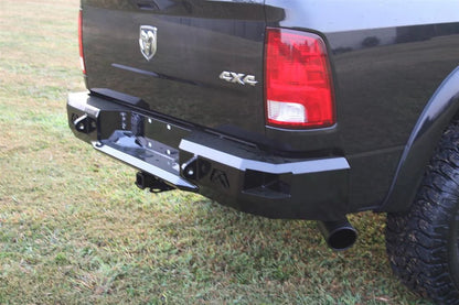 Fab Fours Premium rear bumper on a black Ram 1500, close rear three-quarter view outdoors, showing the angular end cap, Fab Fours logo, and hitch receiver