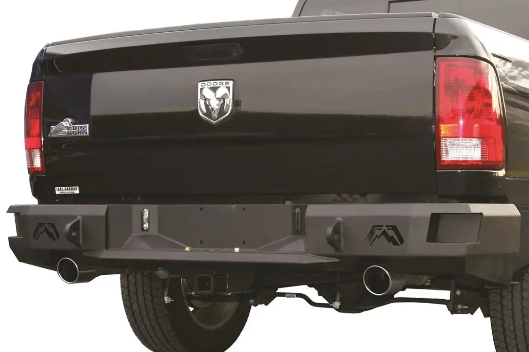 Fab Fours Premium rear bumper on a black Ram 1500, straight-on rear view, showing the logo end caps, center plate recess, and exhaust cutouts