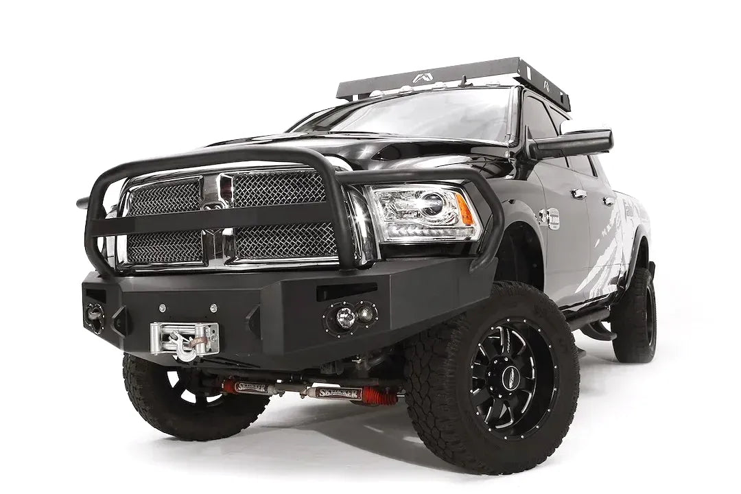 Fab Fours Premium front bumper with full guard on a black Ram 2500, front driver-side three-quarter view, showing the full grille guard, round fog lights, and center winch