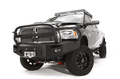 Fab Fours Premium front bumper with full guard on a black Ram 2500, front driver-side three-quarter view, showing the full grille guard, round fog lights, and center winch