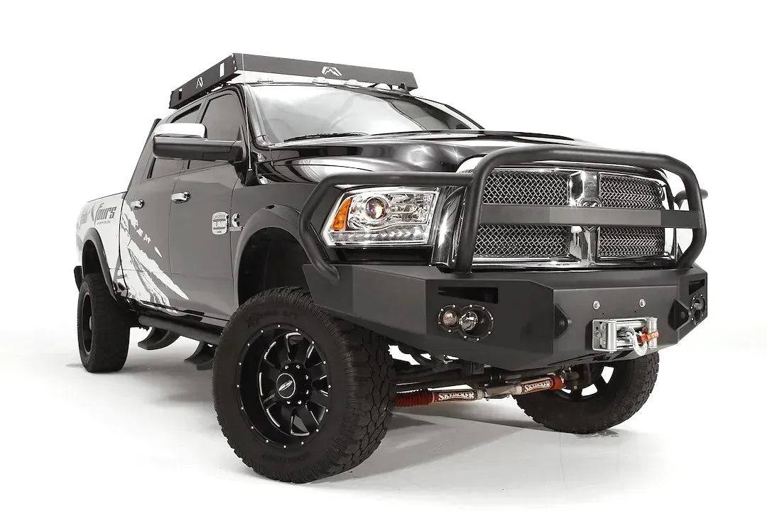 Fab Fours Premium front bumper with full guard on a black Ram 2500, front passenger-side three-quarter view, showing the full grille guard, integrated round lights, and winch opening