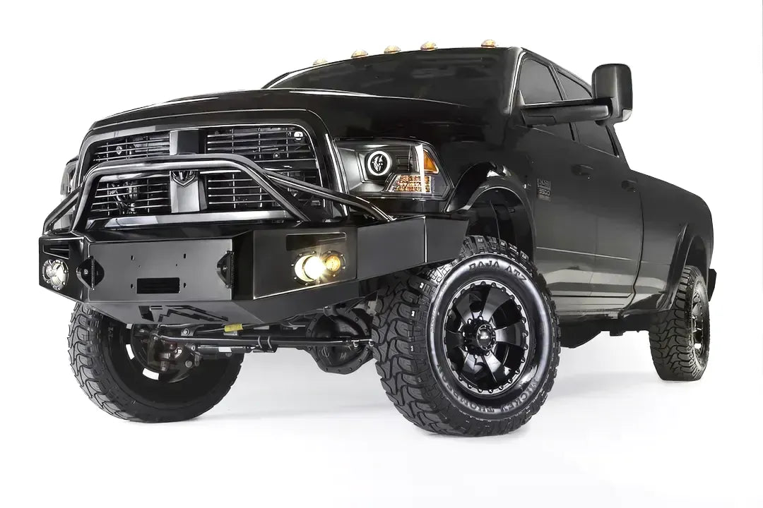 Fab Fours Premium front bumper with pre-runner guard on a black Ram 3500 dually, front driver-side three-quarter view, showing the pre-runner hoop, winch plate, and round fog lights