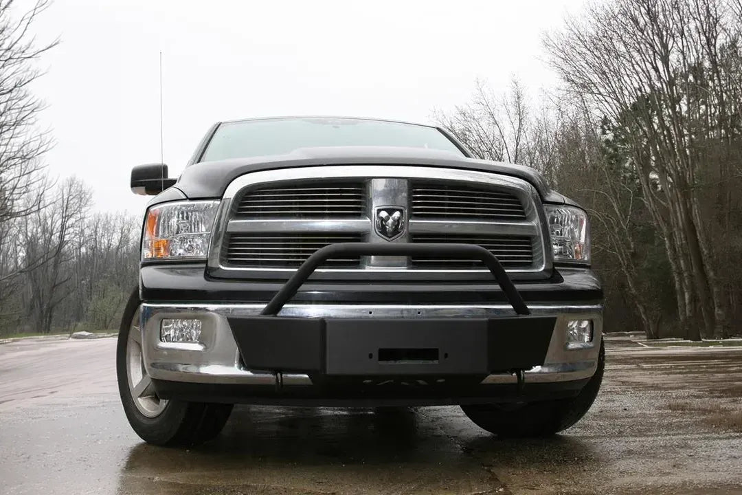 Fab Fours winch mount on a black Ram 1500, straight-on front view outdoors, showing the winch mount plate, tubular hoop, and fairlead opening