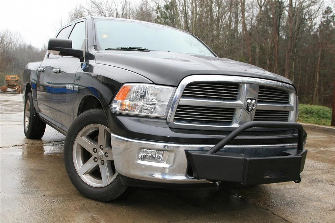 Fab Fours winch mount on a black Ram 1500, front passenger-side three-quarter view outdoors, showing the plated winch mount, tubular hoop, and fairlead opening
