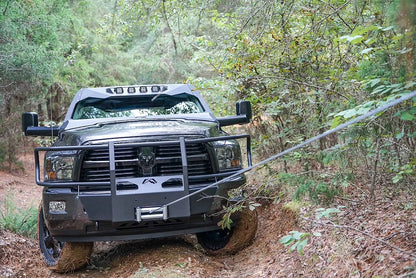 Fab Fours winch mount with full guard on a gray Ram 2500, front view outdoors on a trail, showing the full grille guard, winch with line deployed, and plated mount face