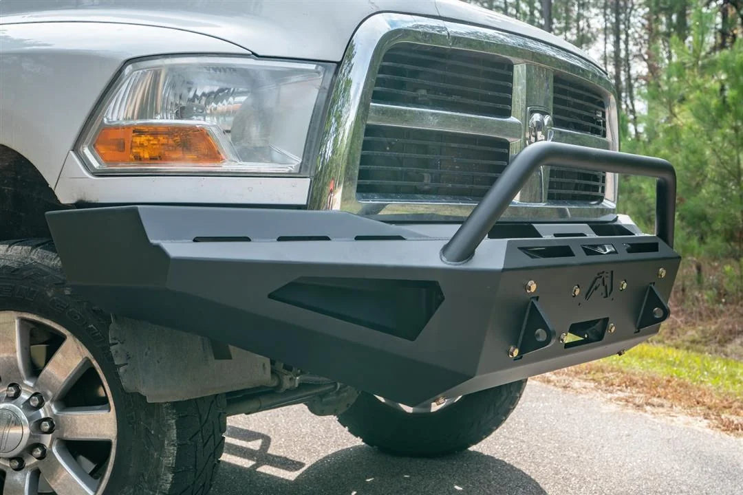 Fab Fours Red Steel front bumper with pre-runner guard on a white Ram 2500, close-up corner view outdoors, showing the pre-runner hoop, D-ring shackle mounts, and slotted top plate