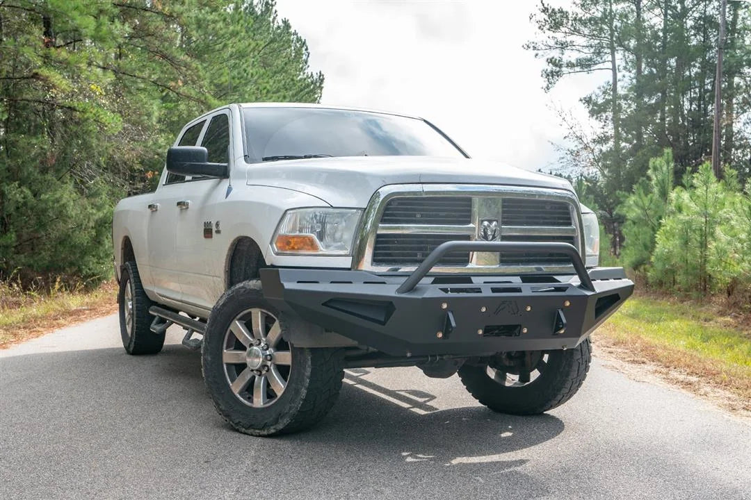 Fab Fours Red Steel front bumper with pre-runner guard on a white Ram 2500, front view outdoors, showing the tubular pre-runner hoop, angular wings, and shackle mounts