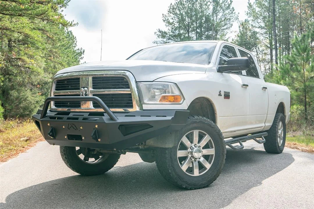 Fab Fours Red Steel front bumper with pre-runner guard on a white Ram 2500, front driver-side three-quarter view outdoors, showing the pre-runner hoop, angular wings, and shackle mounts