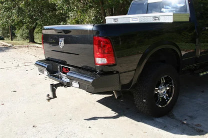 Fab Fours Black Steel rear bumper on a black Ram 1500, rear three-quarter view outdoors, showing the diamond-plate face, integrated lights, and hitch receiver
