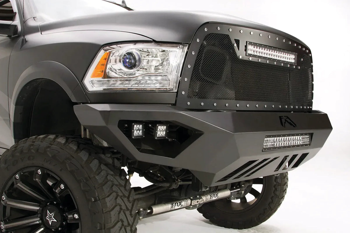 Fab Fours Vengeance front bumper on a gray Ram 2500, close-up corner view, showing the cube light pods, LED light bar opening, and skid plate slots