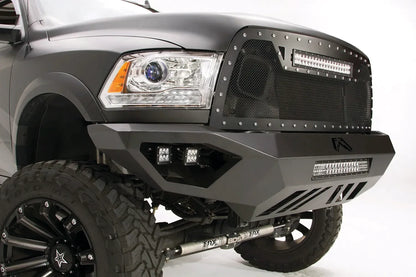 Fab Fours Vengeance front bumper on a gray Ram 2500, close-up corner view, showing the cube light pods, LED light bar opening, and skid plate slots
