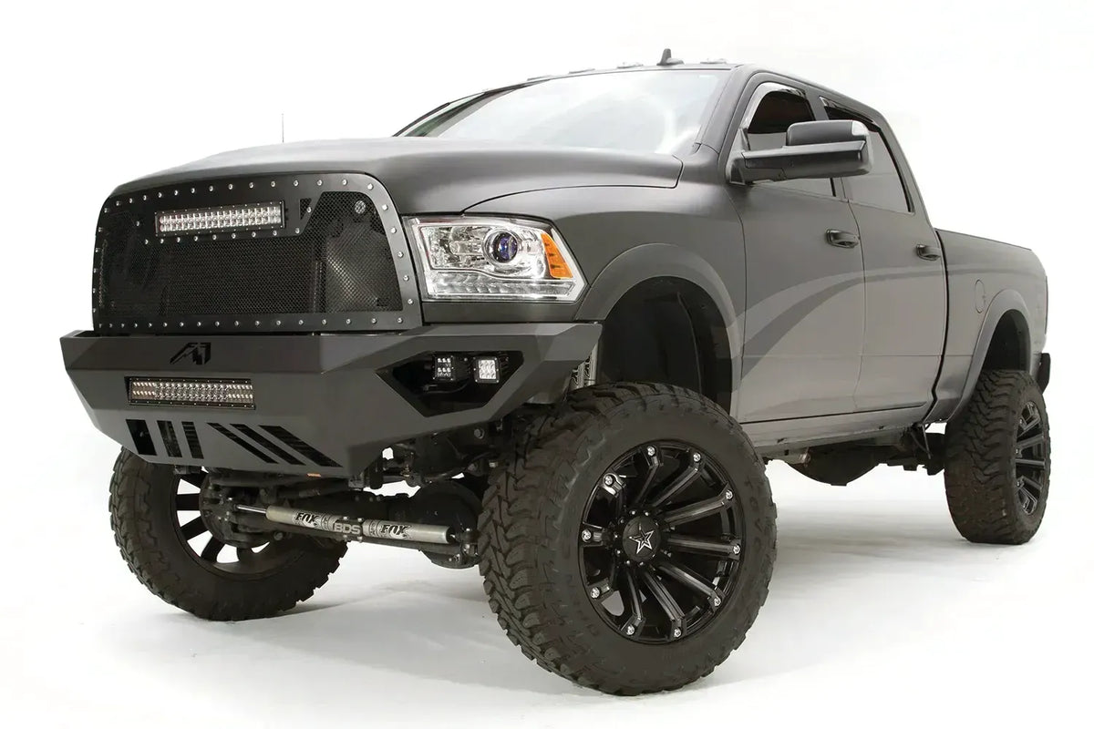 Fab Fours Vengeance front bumper on a gray Ram 2500, front driver-side three-quarter view, showing the angular bumper wing, cube lights, and slotted skid plate