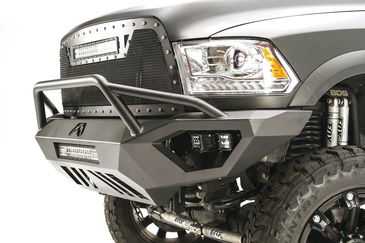 Fab Fours Vengeance front bumper with pre-runner guard on a gray Ram 2500, close-up corner view, showing the tubular pre-runner bar, cube light pods, and slotted skid plate