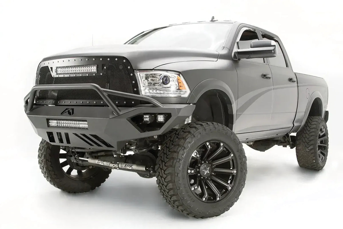 Fab Fours Vengeance front bumper with pre-runner guard on a gray Ram 2500, front driver-side three-quarter view, showing the pre-runner bar, LED light bar, and cube lights