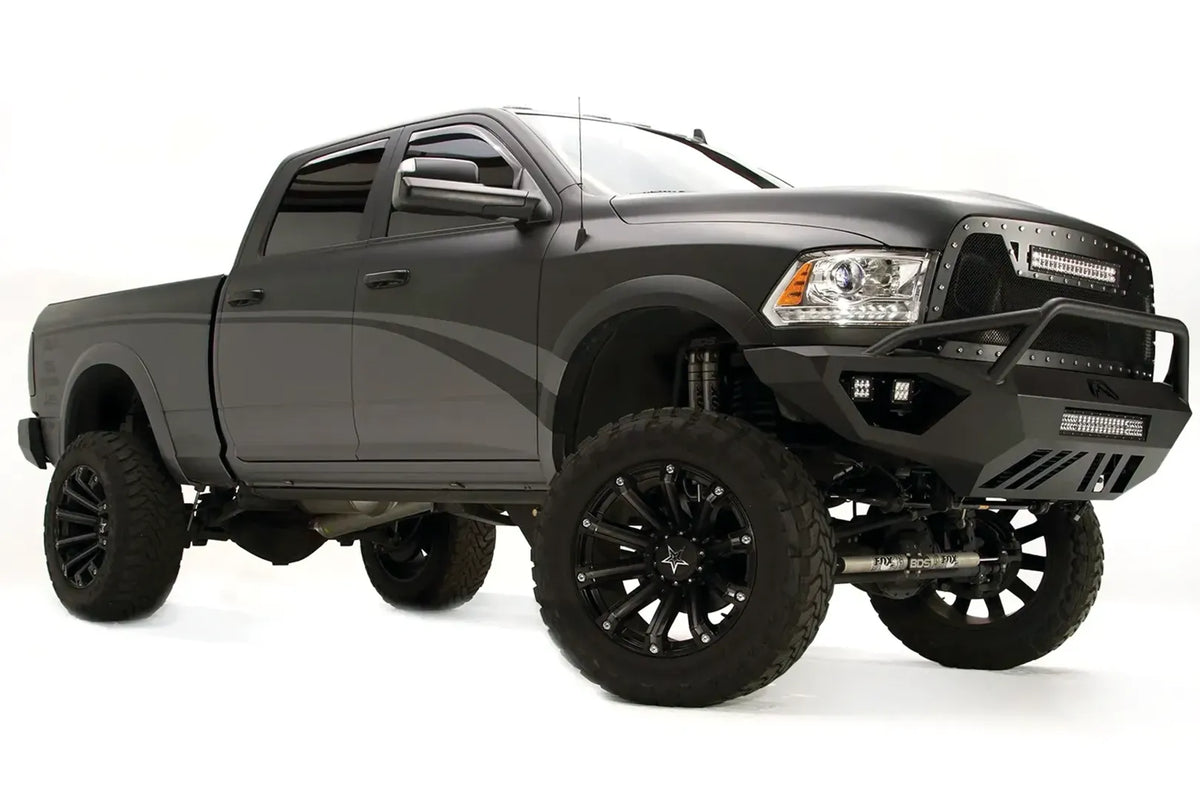Fab Fours Vengeance front bumper with pre-runner guard on a gray Ram 2500, front passenger-side three-quarter view, showing the pre-runner bar, cube light pods, and angular bumper wing