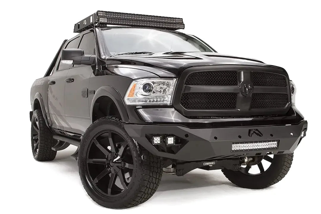 Fab Fours Vengeance front bumper on a black Ram 1500, front driver-side three-quarter view, showing the angular bumper wing, cube lights, and LED light bar