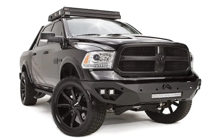 Fab Fours Vengeance front bumper on a black Ram 1500, front driver-side three-quarter view, showing the angular bumper wing, cube lights, and LED light bar